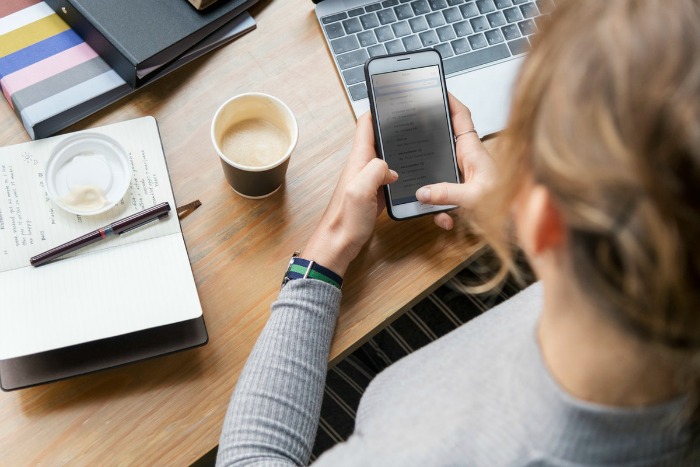 woman using phone by laptop