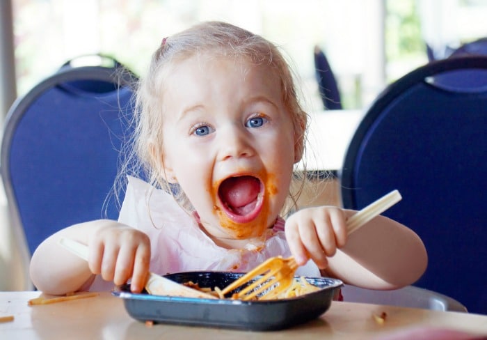 Funny blonde little girl eating pasta and making a mess