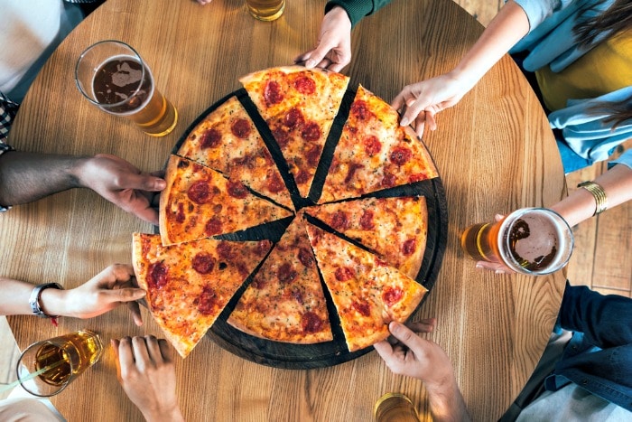 hands reaching for pizza in the middle of a table