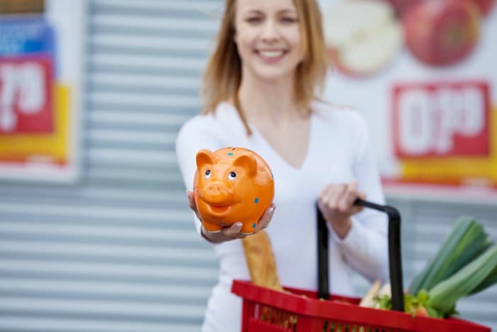 happy young woman showing piggybank while holding shopping basket