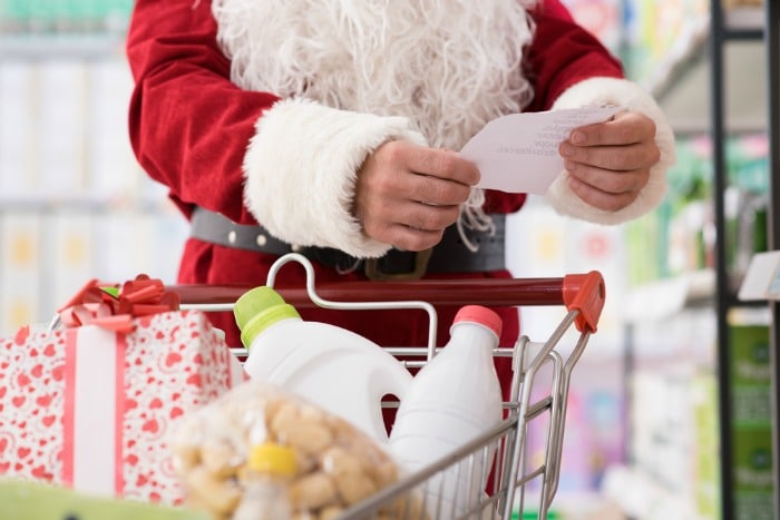 Santa Claus comprando en el supermercado, empuja un carrito de compras lleno y revisa una lista
