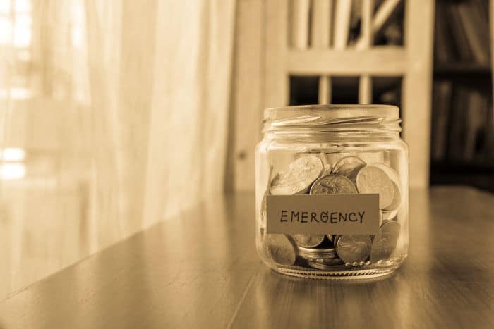 A savings money jar with world coins and emergency word on label