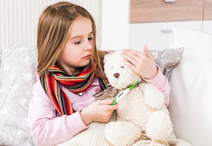 Little ill girl with scarf measuring teddy bear's temperature