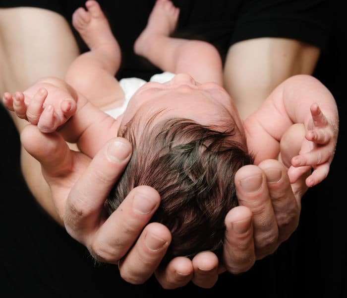 Newborn baby Sleeping on farther Arms on Black Background