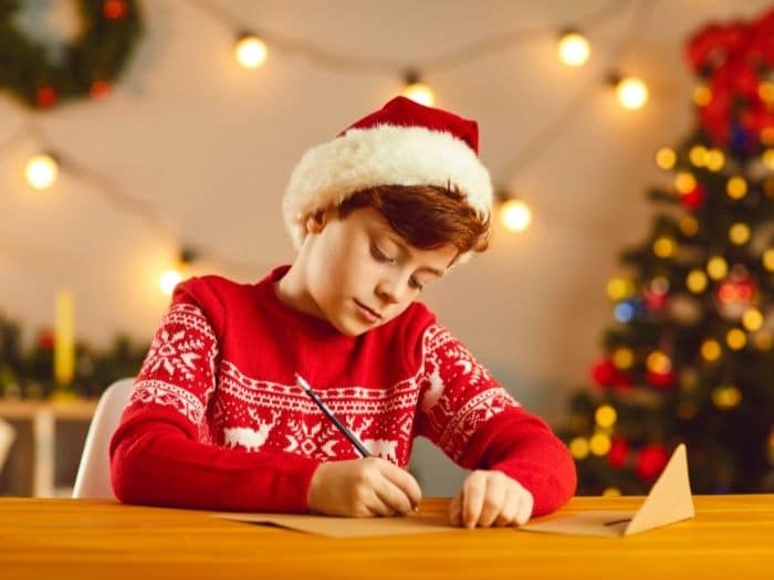 Niño usando un suéter navideño escribiendo una carta 