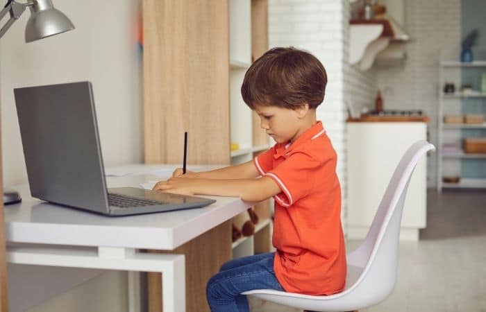 child writing next to laptop