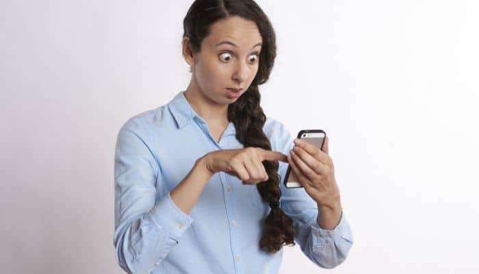 woman holding a mobile phone looking very shocked