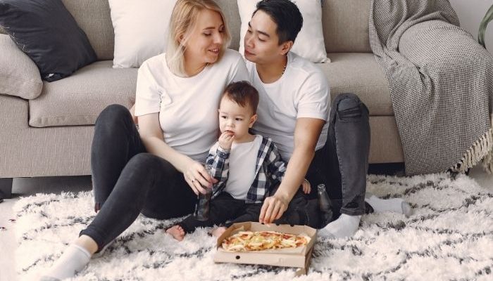 family eating a pizza while sat on a rug in front of a sofa