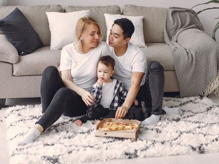 family eating a pizza while sat on a rug in front of a sofa