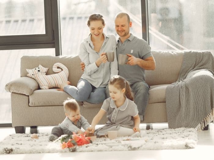 two adults sat on a sofa watching children play