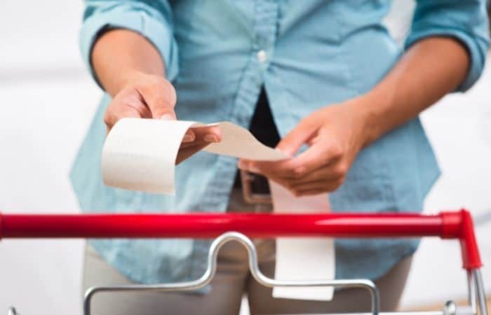 Woman in blue shirt holding a receipt while standing near a supermarket trolley.