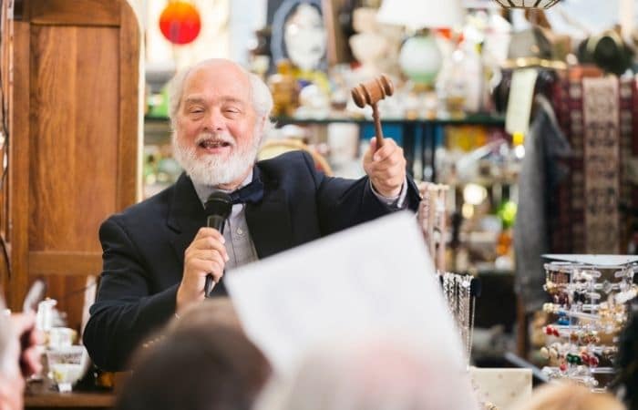 Smiling auctioneer with good for sale behind him.