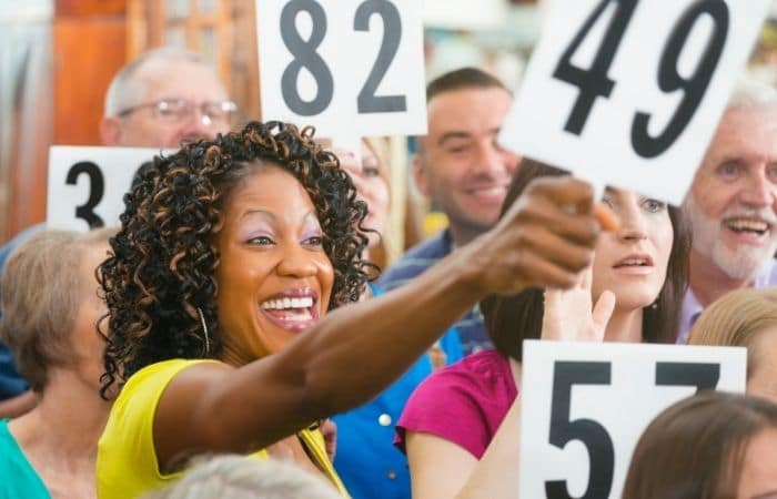 smiling woman in a crowd of people. She is holding an auction number panel.