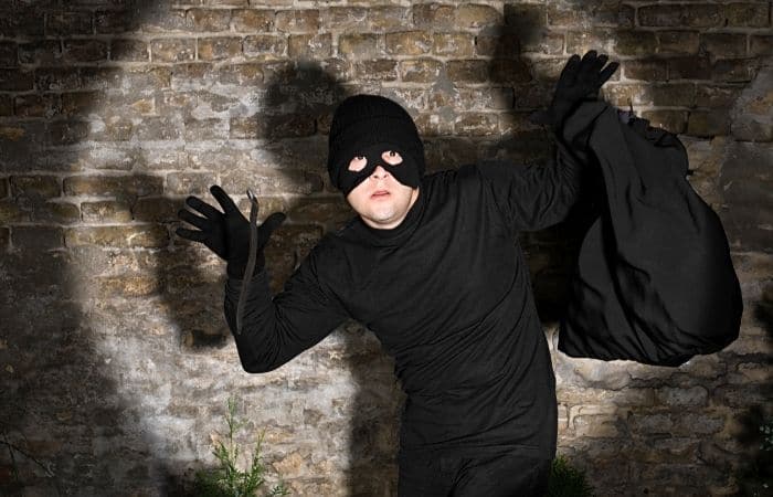man dressed in black clothes with a balaclava, holding a black bag with his hands up