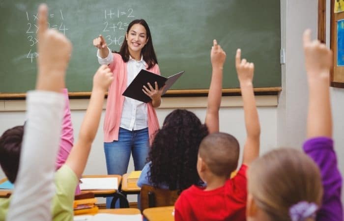 childrens hand up with teacher at front of glass