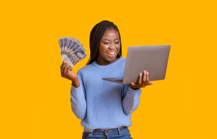 woman smile while holding a laptop with £20 notes in her other hand.