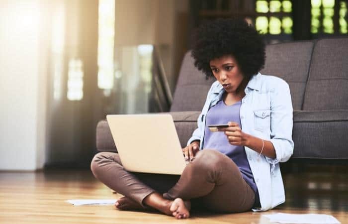 woman sitting on the floor with laptop on her lap and a bank card in her hand