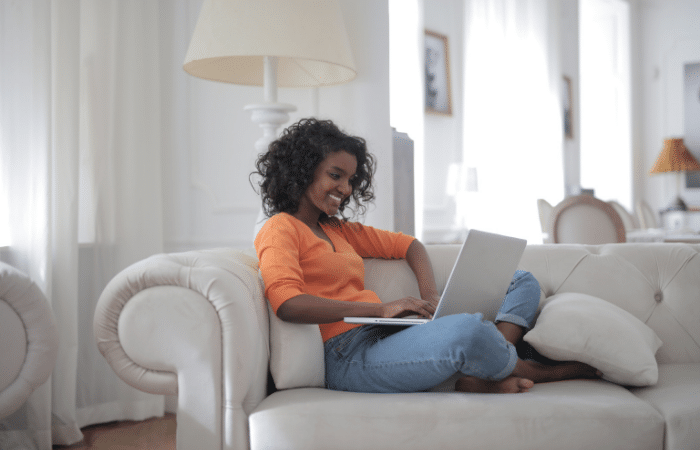 woman sat with legs crossed on a sofa while using a laptop