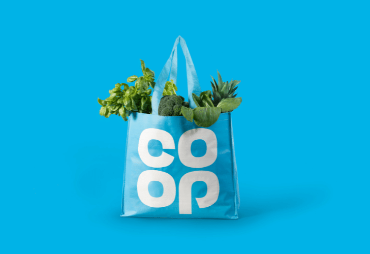Co-op tote bag filled with green vegetables on a blue background