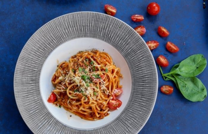 bolognese in a large bowl on a blue background with cut tomatoes and basil