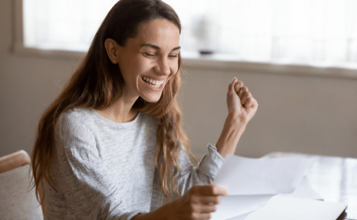 Woman smiling and clenching her fist while looking at a letter
