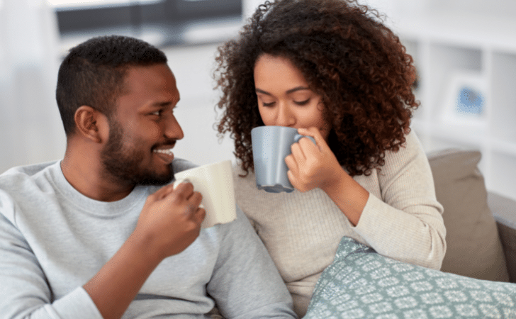 couple drinking coffee on a sofa under a blanket