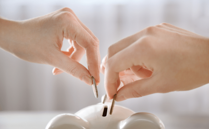 hands putting coins in a piggy bank