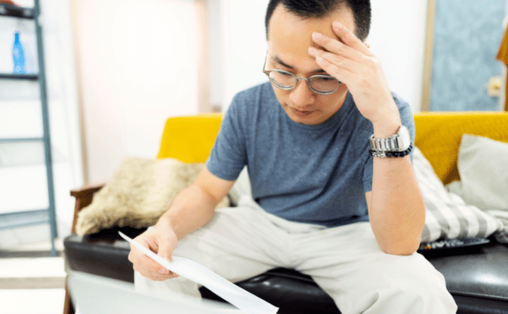 stressed man, holding his head while looking at paperwork