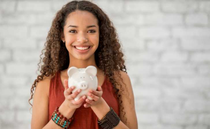 teenage girl smiling and holding a white piggy bank