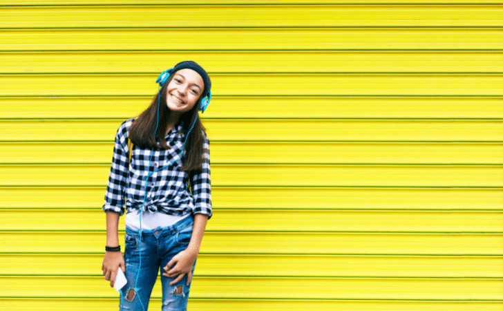 young teenage girl wearing headphones stood in front of a bright yellow wall