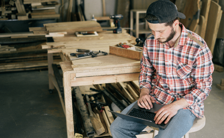 Man in Blue White and Red Plaid Dress Shirt and Gray Denim Jeans Sitting on Brown Stool