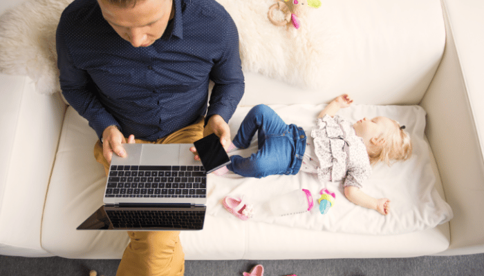 baby sleeping on sofa next to dad with laptop
