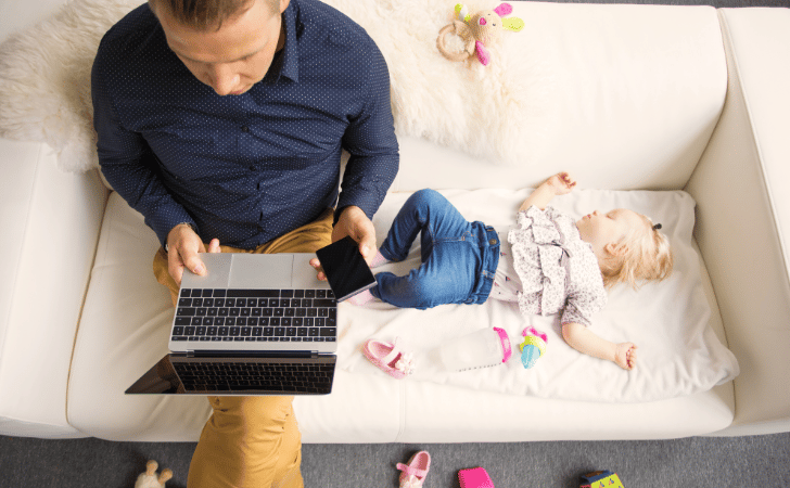 baby sleeping on sofa next to dad with laptop