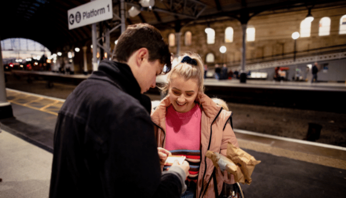 couple looking at tickets at a train station platform during the evening