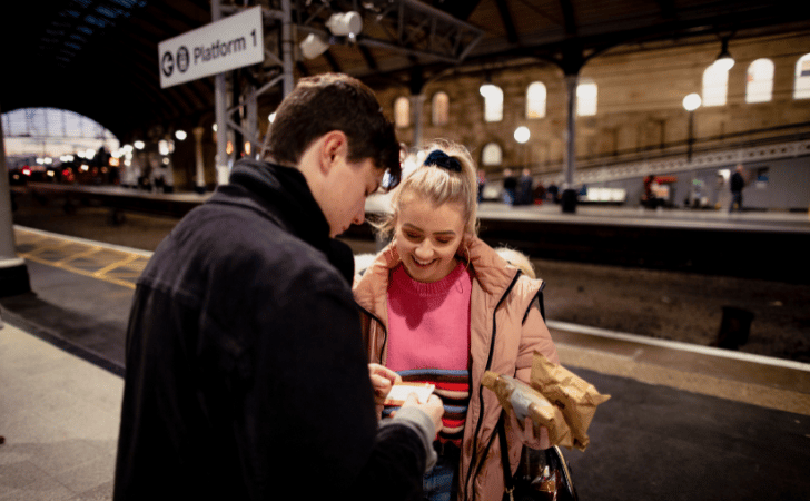 couple looking at tickets at a train station platform during the evening