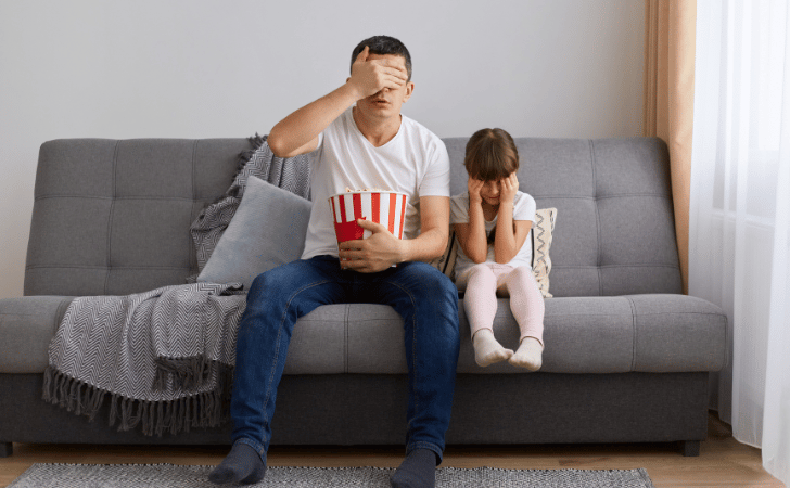 father and daughter eating popcorn on sofa