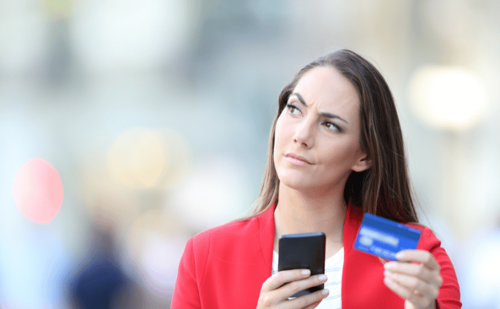 woman in a red blazer looking puzzled, holding a credit card and phone