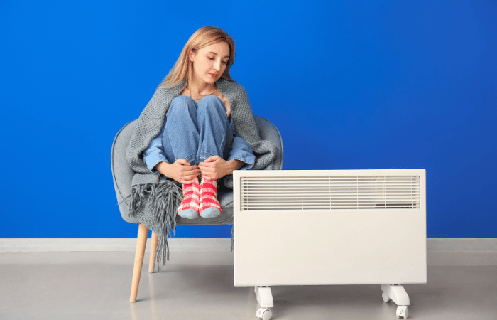 La mujer se sienta en una silla y se cubre con una manta y mira un radiador eléctrico