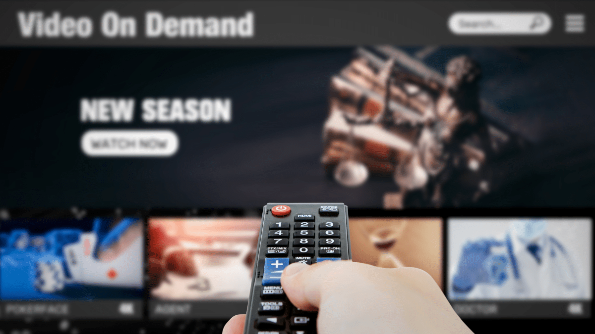 close up of a hand holding a remote control, in front of a blurred TV