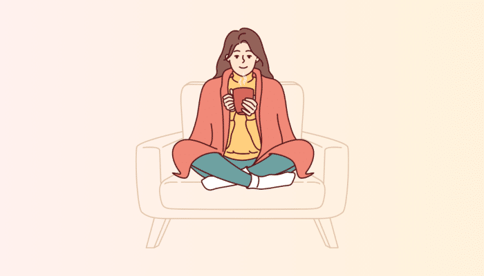 cartoon of a woman sitting in a chair with crossed legs. She has a blanket over her shoulders and is holding a red mug.