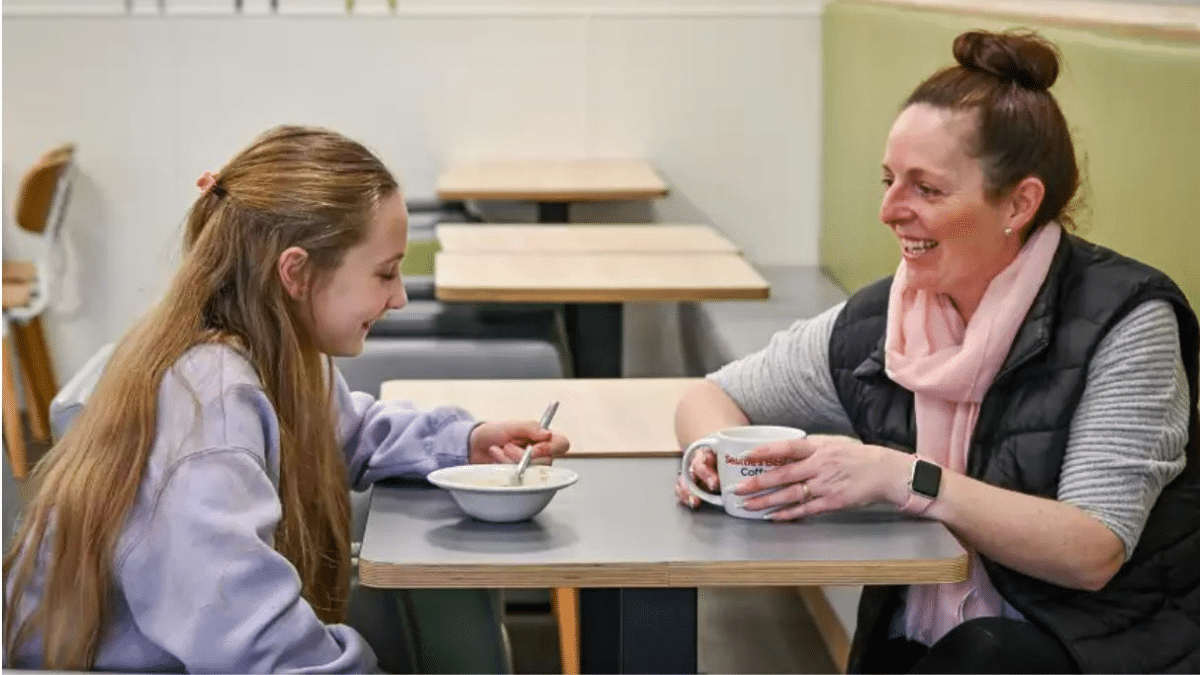woman and child sitting at a table at Asda Cafe. The child is eating a bowl of Quaker porridge and the woman is drinking from a cup.