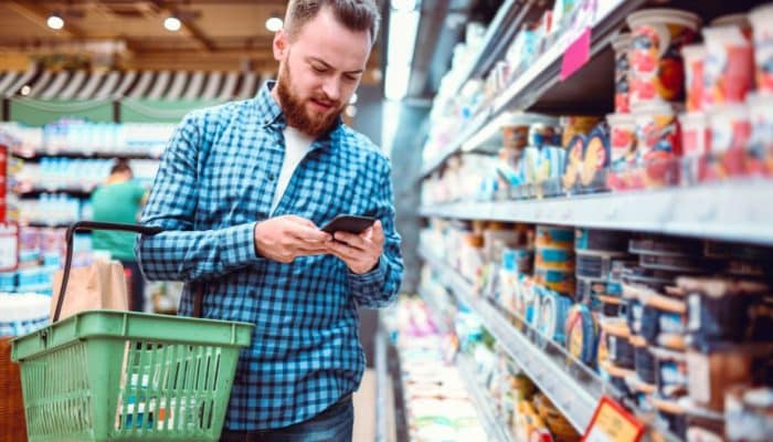 Man in supermarket checking prices on his mobile phone