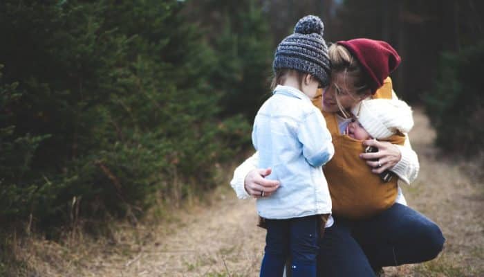 woman crouching on a pathway in a forest. She is holding a baby and talking to a young boy