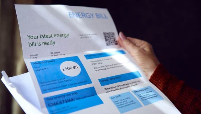 Person in a British home looking worried while checking an energy bill on their phone.