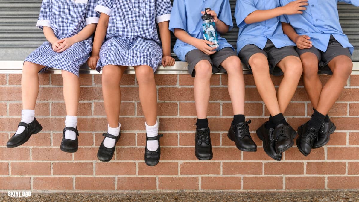 Group of school children sitting on a brick wall wearing school uniforms and black school shoes, showing affordable footwear options for the new term.