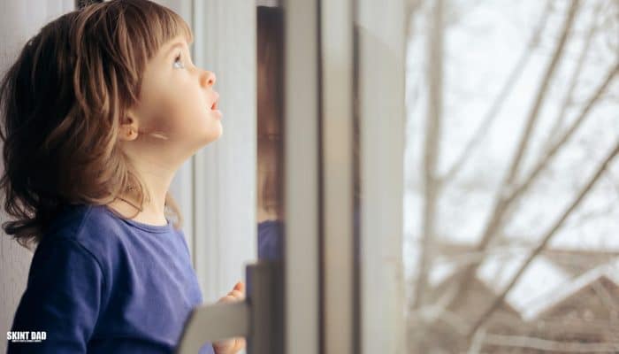Child standing by a window at home in soft winter light, looking outside