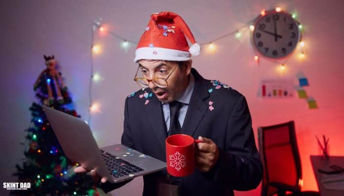 Office worker in a Santa hat looking surprised at a laptop while holding a mug, with Christmas decorations in the background