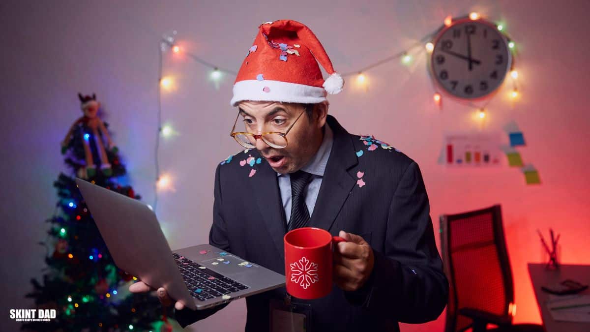 Office worker in a Santa hat looking surprised at a laptop while holding a mug, with Christmas decorations in the background