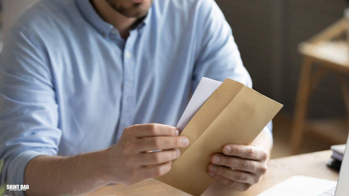 Man opening a household bill envelope in a UK home, showing the quiet stress of money worries.