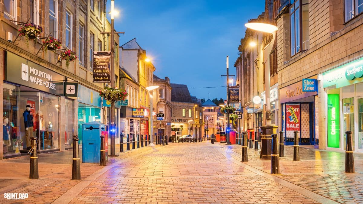 A quiet UK high street with local shops, showing everyday life for people balancing benefits and small side hustles.